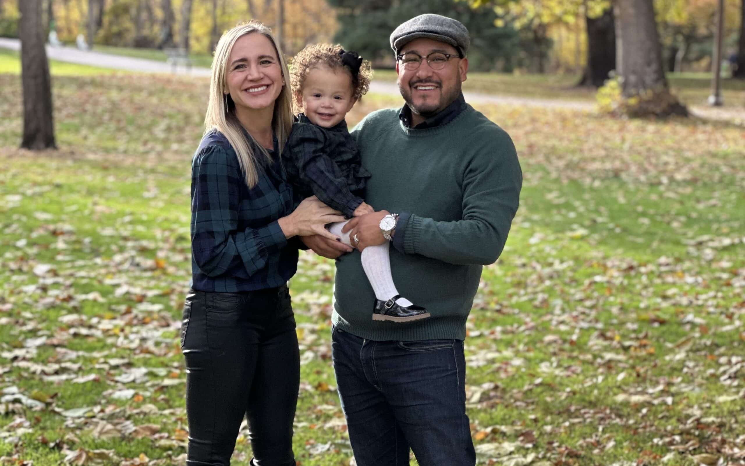 Shows our provider Erin Renak, PA-C with her husband and  young daughter posing together and smiling in a field with leaves and trees